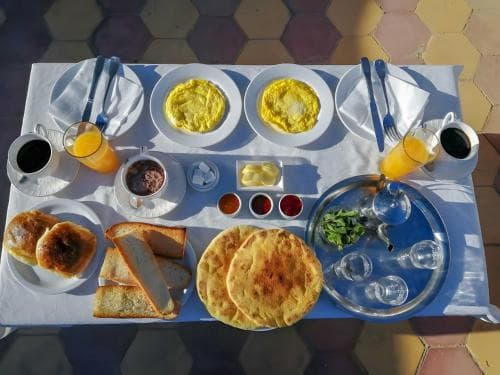 A vibrant outdoor breakfast table set on a tiled patio, featuring omelets, breads, cheese, and fresh juice, evokes a cozy morning ambiance ideal for travelers seeking a local culinary experience.