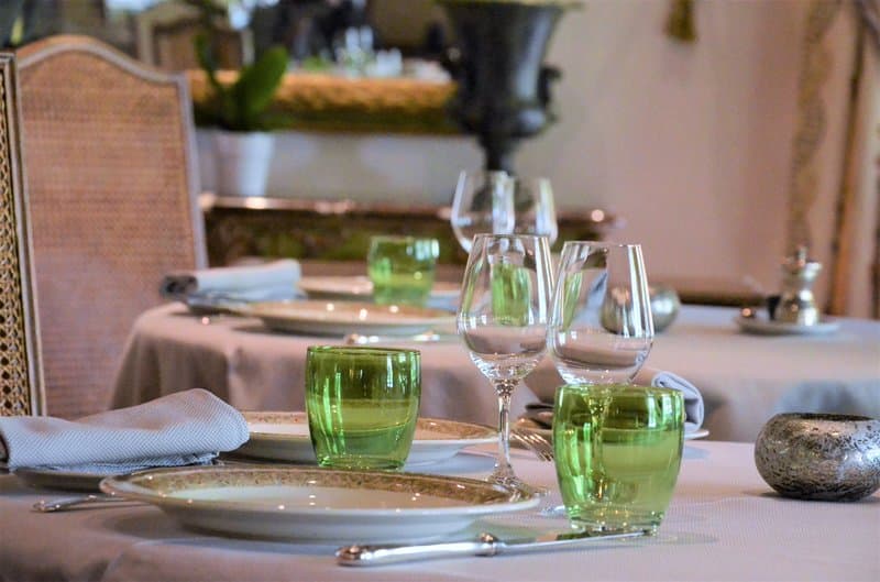 An elegantly set dining table with green glassware and fine silverware invites travelers to enjoy a sophisticated meal in a serene restaurant setting.