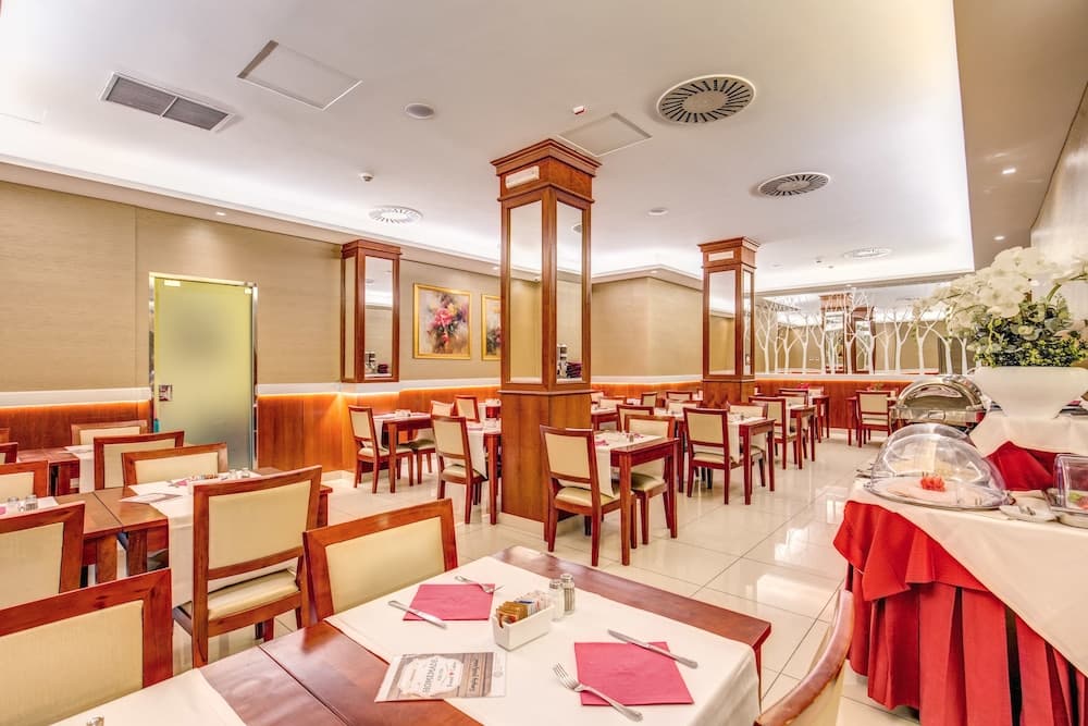 A cozy indoor restaurant with neatly arranged tables, red accents, and elegant decor offers a welcoming atmosphere for travelers seeking a comfortable dining experience.