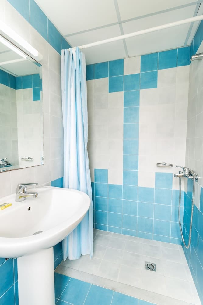 A serene hotel bathroom features blue and white tiled walls, a pristine sink, a shower curtain, and a modern faucet, ideal for travelers seeking cleanliness and comfort.