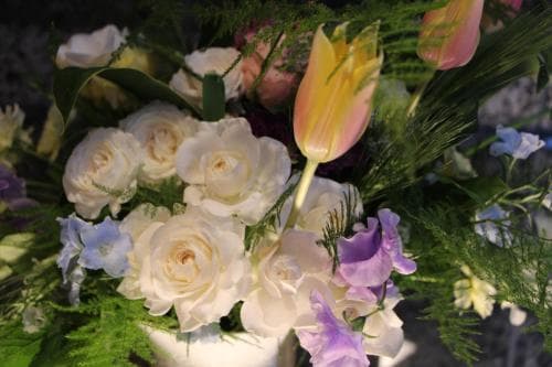 A serene floral arrangement featuring white roses, purple blooms, and a vibrant tulip amidst lush greenery creates an elegant centerpiece perfect for wedding decor or event planning.