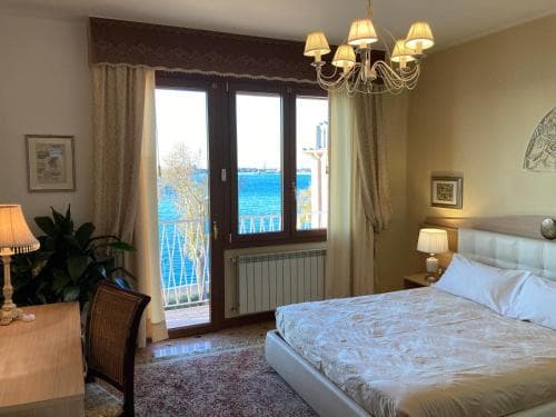 A cozy bedroom with a serene ocean view through glass doors, featuring elegant decor like a chandelier and plush bedding, ideal for a relaxing seaside getaway.