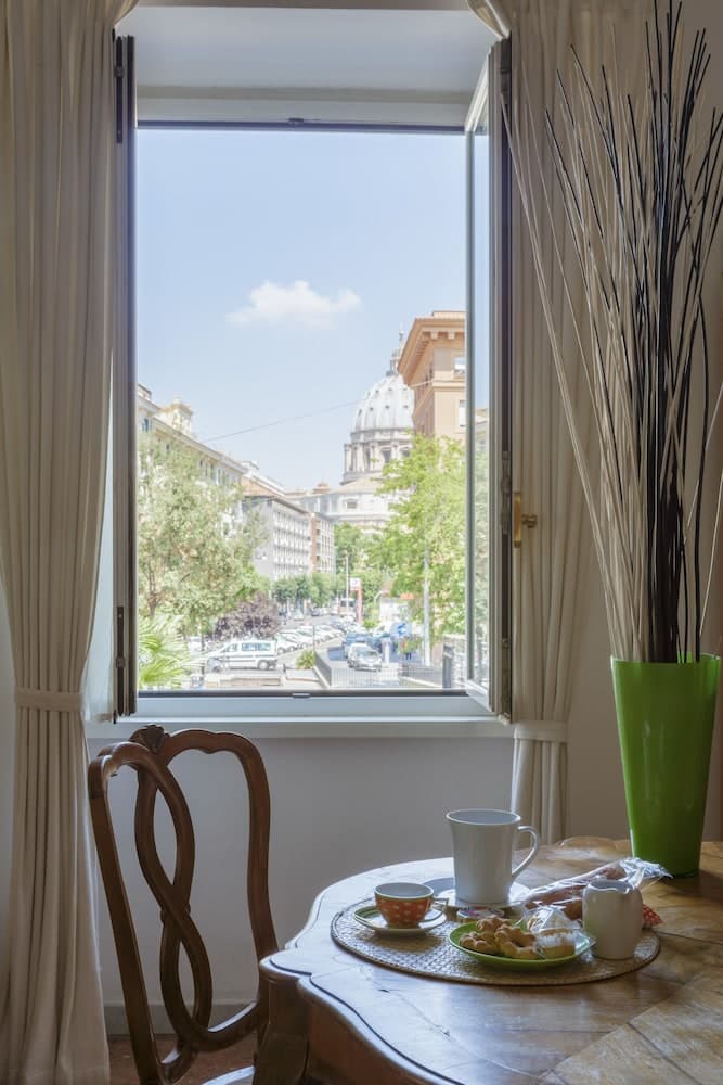 A cozy breakfast nook with a wooden table set for tea overlooks a vibrant cityscape featuring historic architecture and lush greenery, ideal for travelers seeking a serene morning view in an urban retreat.