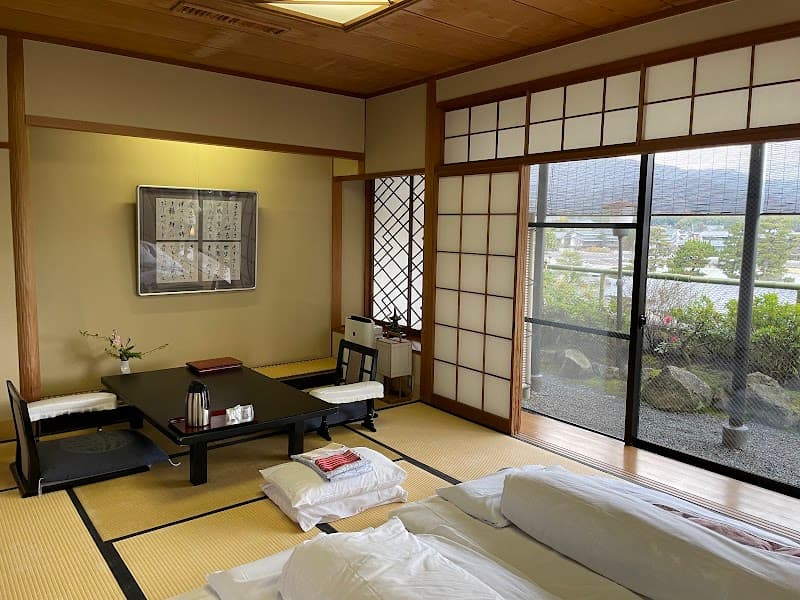 A serene traditional Japanese tatami room with sliding shoji screens offers a tranquil view of a garden and distant mountains, ideal for travelers seeking cultural immersion in Kyoto.