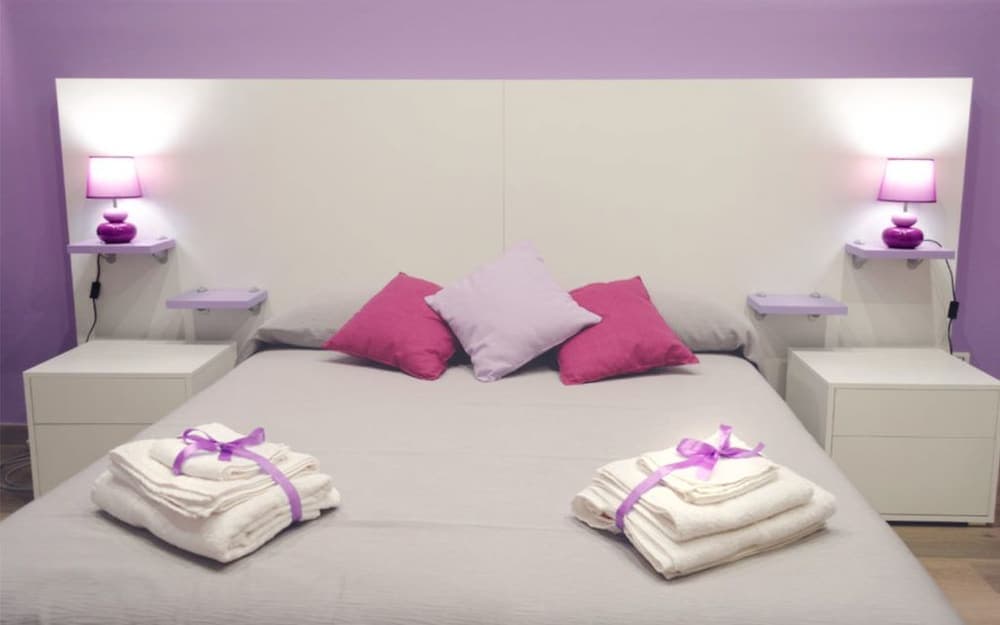 A cozy hotel bedroom with purple accents features neatly arranged towels on the bed, soft lighting from bedside lamps, and a serene ambiance ideal for relaxation and leisure travel.