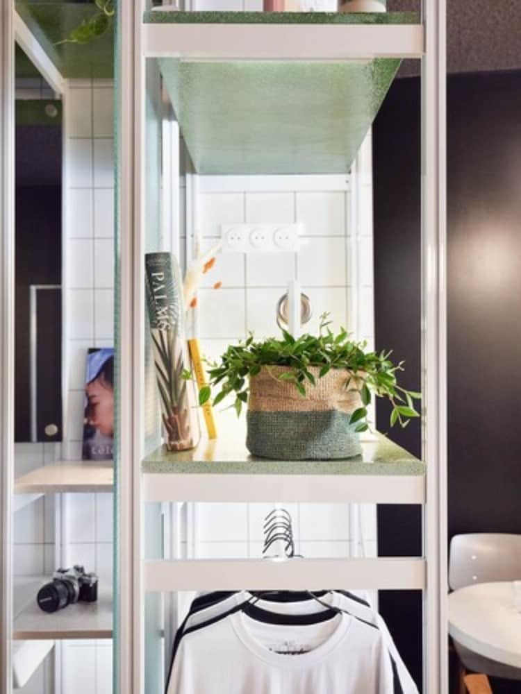 A cozy apartment corner features a stylish shelving unit with greenery, books, and clothing, creating a serene and organized space ideal for home office or personal retreat inspiration.