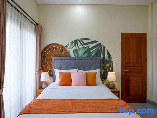A cozy hotel bedroom features a vibrant tropical-themed headboard, soft lighting, and warm orange accents, creating an inviting atmosphere ideal for travelers seeking relaxation.
