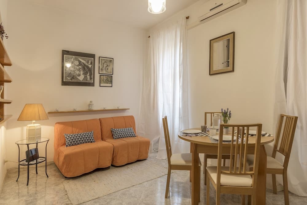 A cozy apartment living space features an orange sofa, wooden dining set, soft lighting, and framed artwork, ideal for travelers seeking a comfortable and inviting short-term rental.