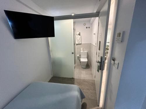 A cozy hotel room with a neatly made bed, mounted TV, and an open door leading to a clean bathroom, ideal for travelers seeking comfort and convenience.