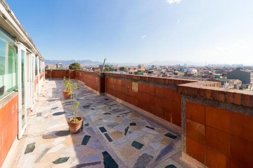 A serene rooftop terrace with mosaic-tiled flooring, potted plants, and a panoramic cityscape view offers an ideal spot for travelers seeking relaxation and urban exploration.