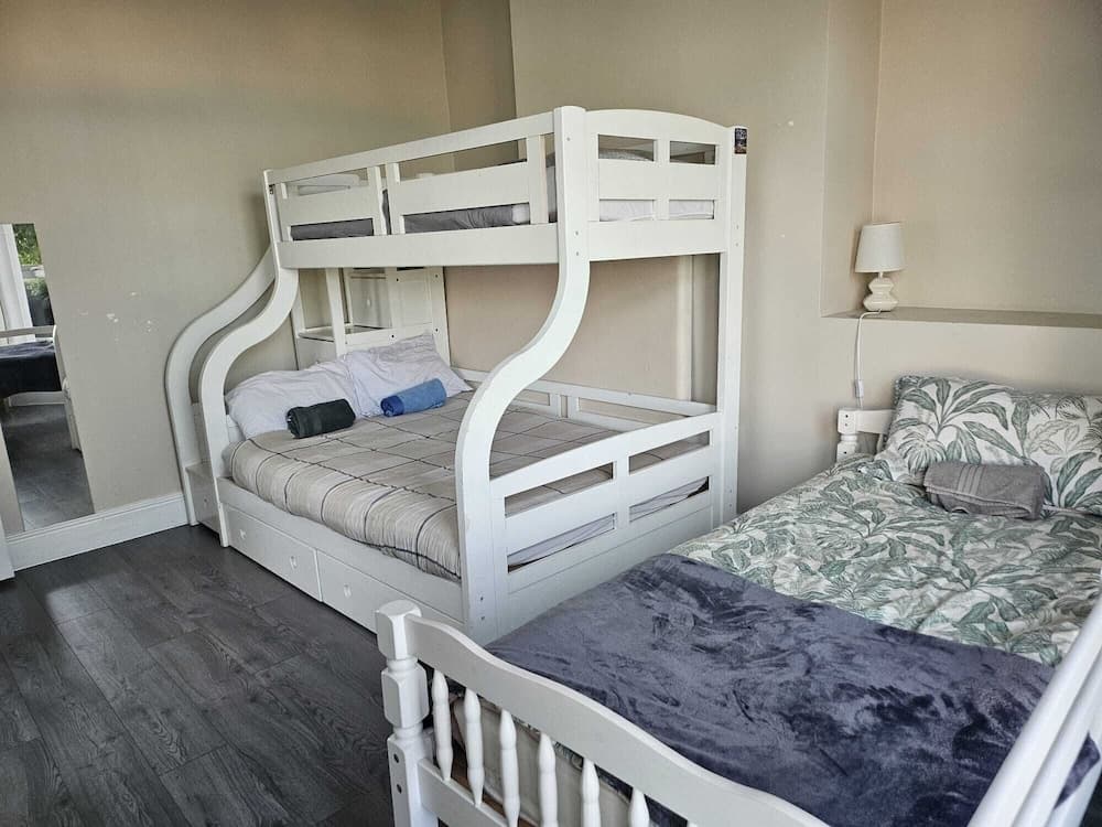 A cozy family-friendly bedroom features a white bunk bed with storage drawers and a single bed adorned with tropical-patterned bedding, ideal for vacation rentals or family stays.