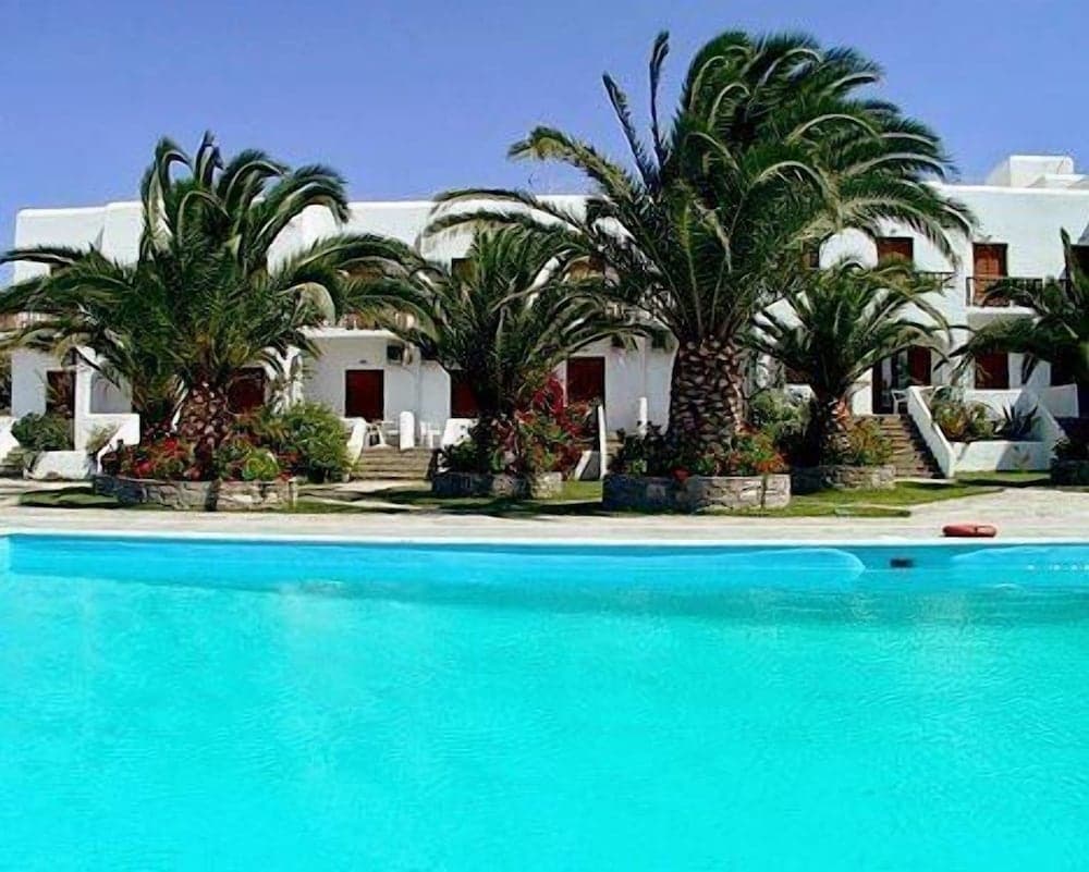 A serene tropical resort features a vibrant turquoise pool surrounded by lush palm trees and white buildings, ideal for a relaxing vacation getaway.