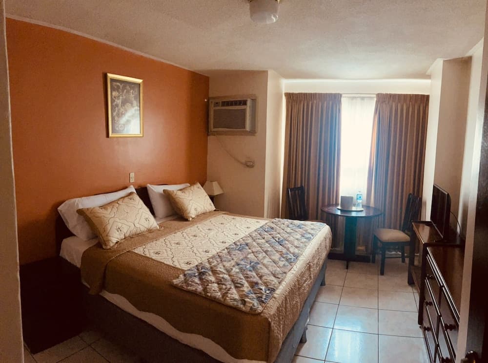 A cozy hotel room with an orange accent wall, neatly made bed, small dining area by the window, and a warm ambiance is ideal for travelers seeking comfort and convenience.