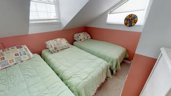 A cozy attic bedroom with soft green bedding on twin beds under slanted ceilings, featuring playful wall decor, ideal for family-friendly vacation rentals.