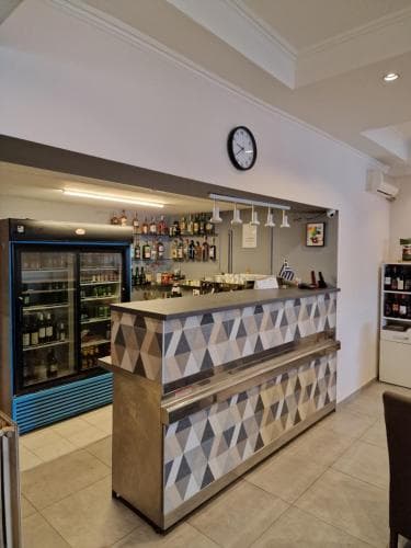 A cozy bar area with a geometric-patterned counter, stocked shelves of beverages, and a modern clock on the wall creates an inviting atmosphere ideal for travelers seeking a relaxed spot to unwind.