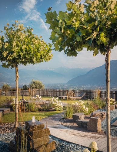 A serene garden with lush greenery, stone pathways, and mountain views offers a tranquil retreat, ideal for relaxation and nature photography.