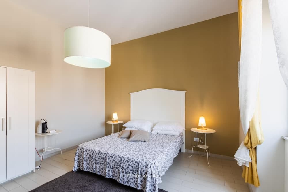 A cozy bedroom with a mustard yellow accent wall, white furnishings, and soft lighting creates a serene atmosphere, ideal for travelers seeking a tranquil retreat.