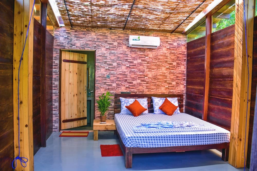 A cozy, rustic cabin bedroom with a wooden bed, brick-patterned walls, and a thatched roof creates a serene retreat, ideal for travelers seeking a tranquil escape in nature.