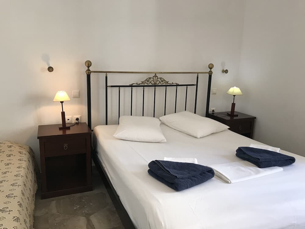 A cozy hotel room features a neatly made bed with white linens and blue towels, flanked by wooden nightstands with lamps, creating a serene atmosphere ideal for travelers seeking relaxation.