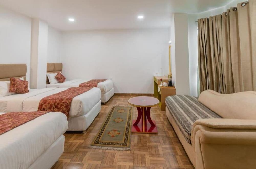 A cozy hotel room features two neatly made beds, a comfortable sofa, and warm wooden flooring, creating an inviting atmosphere ideal for travelers seeking relaxation and comfort.