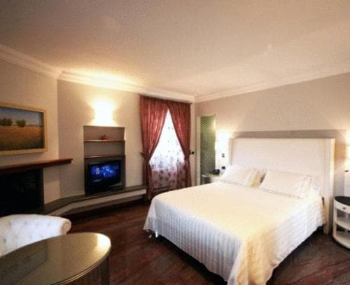 A cozy hotel room features a neatly made bed, warm lighting, a fireplace with a TV, and elegant curtains, creating an inviting atmosphere ideal for travelers seeking comfort and relaxation.