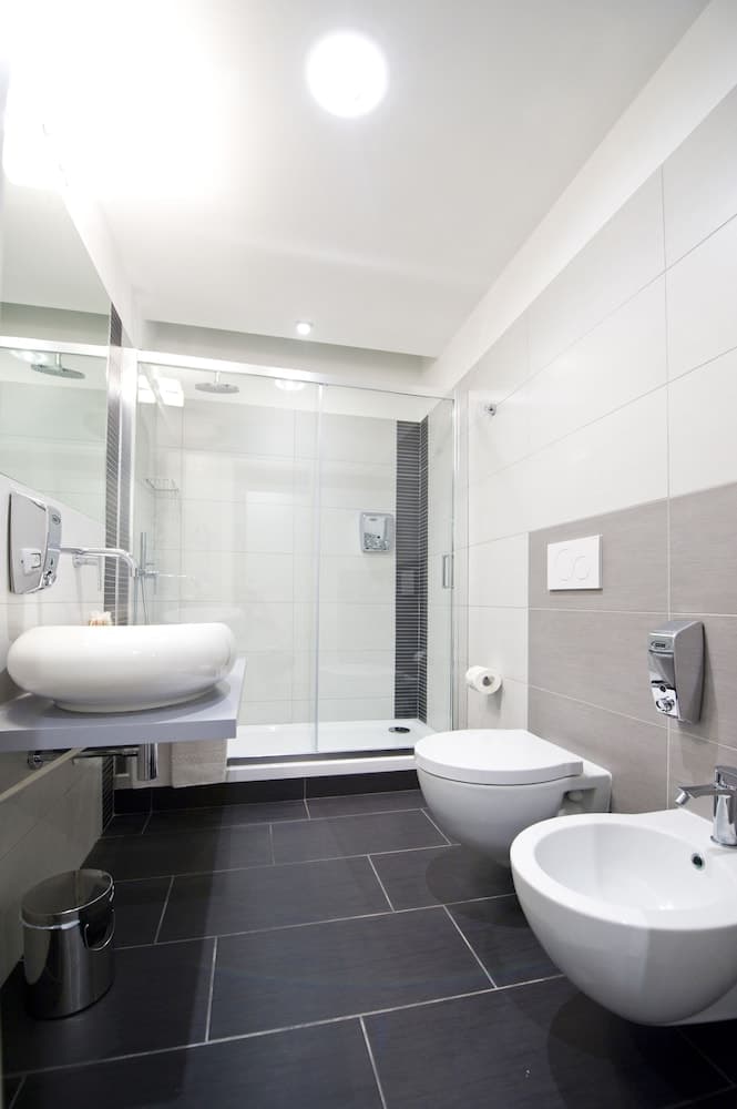 A modern bathroom with sleek black tiles, white fixtures including a vessel sink and bidet, a glass-enclosed shower, and minimalist decor creates a clean and serene atmosphere ideal for travelers seeking comfort and style in accommodations.