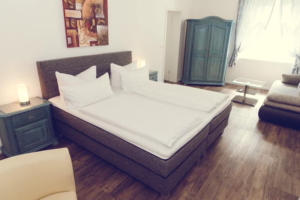 A cozy hotel room features a neatly made bed with white linens, vintage-style furniture, and soft lighting, creating a serene atmosphere ideal for relaxation and leisure travel.