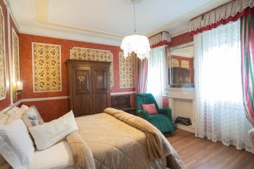 A cozy bedroom with ornate red walls, patterned decor, and soft lighting creates an inviting atmosphere, perfect for travelers seeking a charming and comfortable stay in a boutique hotel.
