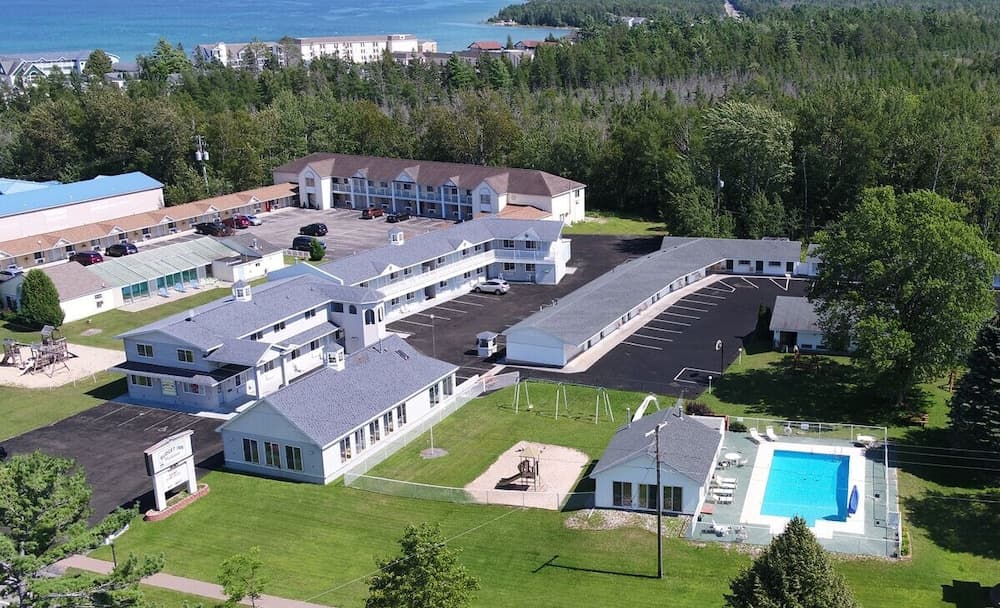 An aerial view of a cozy motel complex surrounded by lush greenery and a serene waterfront, featuring amenities like a swimming pool and playground, ideal for family vacations seeking relaxation and nature proximity.