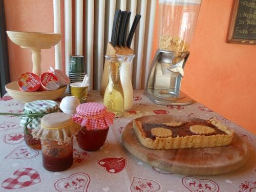 A cozy kitchen scene features a rustic tart on a wooden board surrounded by jars of homemade preserves, a blender, and a checkered tablecloth, evoking a warm, homely atmosphere ideal for culinary enthusiasts exploring local food culture.
