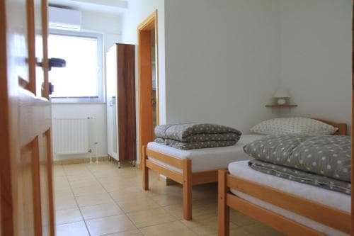 A cozy, minimalist bedroom with two wooden beds, tiled flooring, and natural light from a window, ideal for budget-friendly travelers seeking simple accommodations.