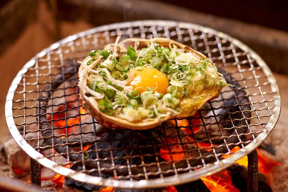 A vibrant egg nestled in a shell atop a sizzling grill, garnished with fresh greens, evokes a cozy, rustic dining experience perfect for culinary travelers exploring traditional cooking methods.