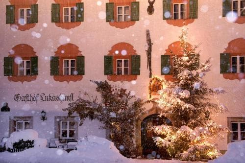 A cozy, snow-covered traditional European inn adorned with festive lights and a decorated Christmas tree creates a warm, inviting atmosphere perfect for winter getaways.