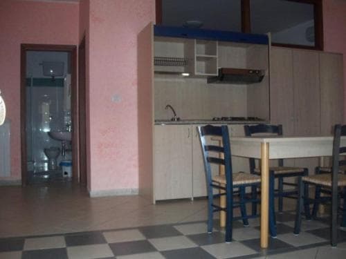 A cozy apartment kitchen with a checkered floor, wooden dining table, blue chairs, and a visible bathroom through an open door, ideal for travelers seeking a homey and functional stay.