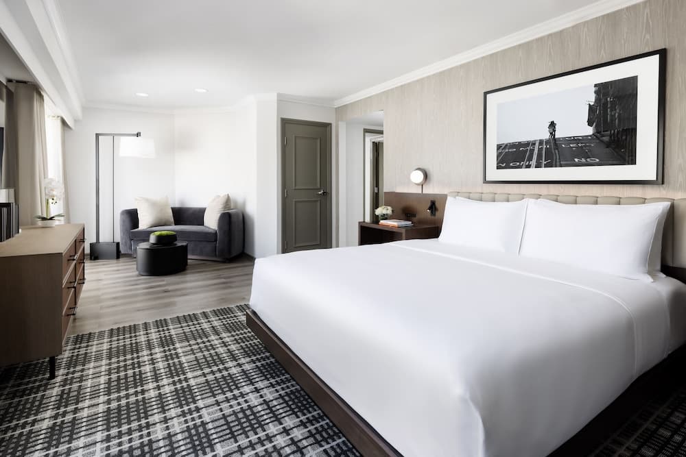A modern hotel suite features a cozy bedroom with a neatly made bed, a stylish gray sofa, and contemporary decor, ideal for travelers seeking comfort and elegance during their stay.