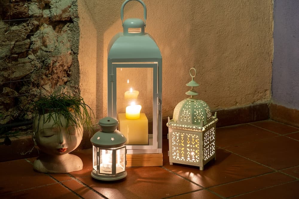 A cozy outdoor patio corner features glowing lanterns and a serene face planter, creating an inviting ambiance perfect for evening relaxation.