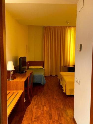 A cozy hotel room with warm yellow curtains, wooden furniture, and a desk setup invites travelers seeking comfort and functionality for a relaxing stay.