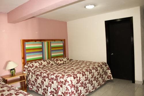 A cozy hotel room features a neatly made bed with a colorful headboard against a soft pink wall, creating a welcoming atmosphere ideal for travelers seeking comfort and relaxation.