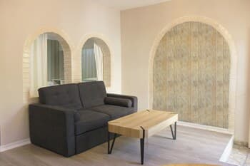 A cozy living room with arched doorways, a sleek gray sofa, and a wooden coffee table exudes a serene ambiance, ideal for travelers seeking a tranquil accommodation experience.
