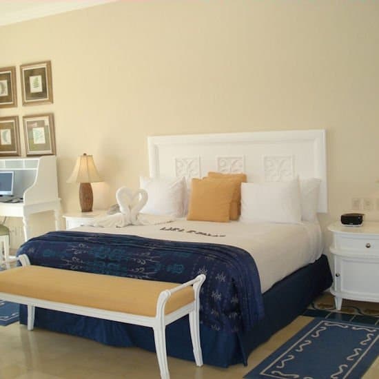 A cozy hotel room features a neatly made bed adorned with a decorative towel swan, framed artwork on the walls, and a white desk with a lamp, ideal for travelers seeking comfort and relaxation.