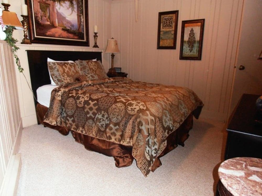 A cozy bedroom with a patterned bedspread, framed artwork, and soft lighting creates an inviting atmosphere ideal for travelers seeking comfort and relaxation.