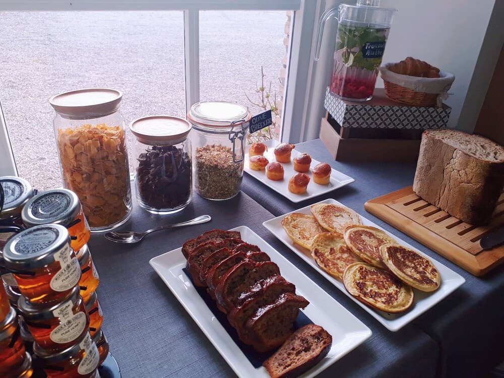 A cozy breakfast spread featuring fresh breads, pancakes, jams, and cereals on a table by a window overlooking a serene outdoor view, perfect for a relaxing morning getaway.