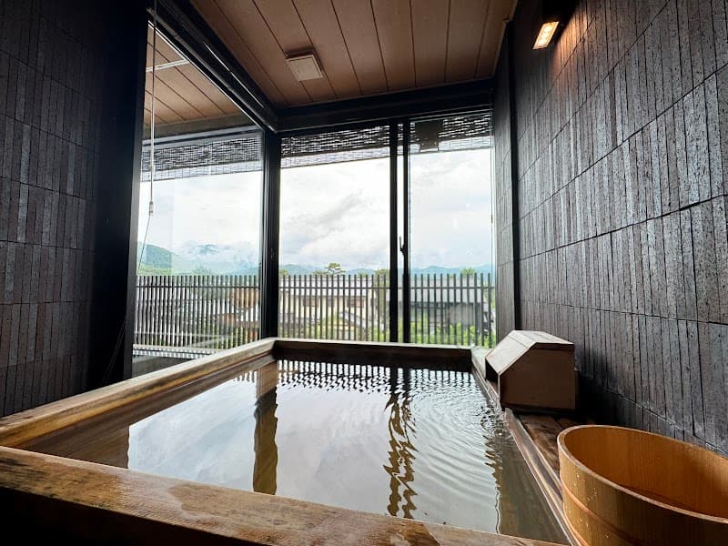 A serene indoor onsen bath offers a tranquil view of distant mountains through large windows, ideal for relaxation in Kyoto's Arashiyama area.