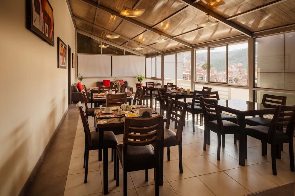 A cozy restaurant with wooden tables, modern art on the walls, and large windows offering scenic views of a bustling cityscape, ideal for travelers seeking a relaxing dining experience with a view.
