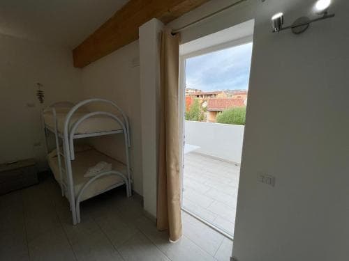 A cozy hostel room with a bunk bed opens to a serene balcony view of tiled rooftops under a partly cloudy sky, ideal for budget travelers seeking simplicity and charm.