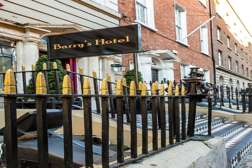 A charming urban hotel entrance features a black railing with gold-tipped posts leading to Barry's Hotel, set against a backdrop of classic brick and white architecture, ideal for travelers seeking a historic and elegant stay.