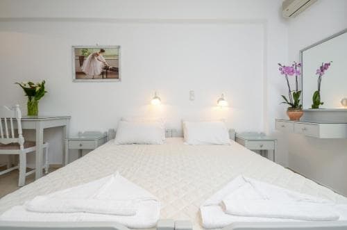 A serene hotel room features a neatly made bed, white decor, fresh flowers, and soft lighting, ideal for travelers seeking a peaceful retreat.