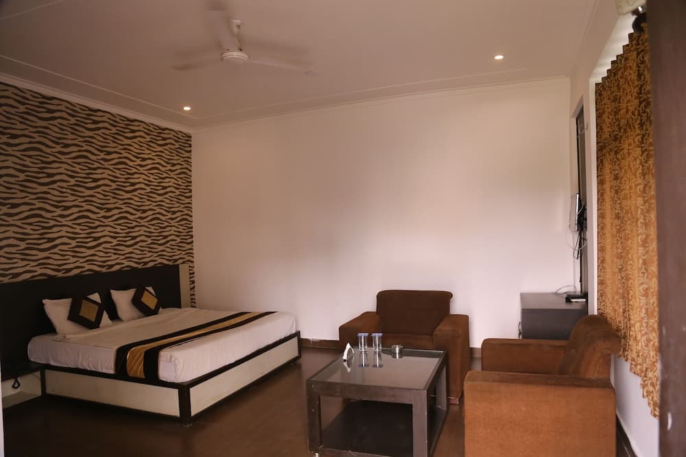 A cozy hotel room features a neatly made bed against a zebra-patterned wall, a comfortable seating area with brown armchairs, a glass coffee table, and warm lighting, ideal for travelers seeking relaxation and comfort.