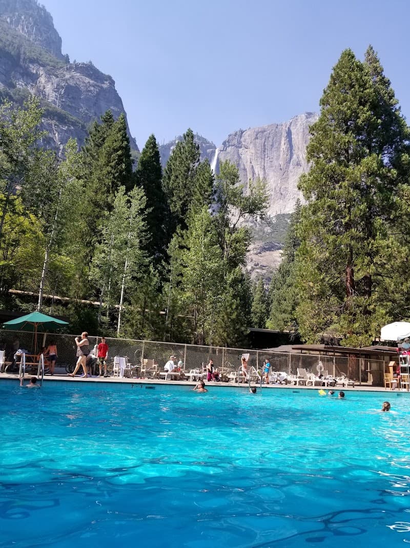 A vibrant pool scene at Yosemite Valley Lodge offers a refreshing retreat against the backdrop of towering granite cliffs and lush pine trees, ideal for travelers seeking relaxation in nature's embrace.