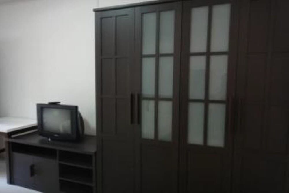 A cozy bedroom corner features a dark wooden wardrobe with frosted glass doors and a small CRT television on a matching cabinet, ideal for travelers seeking simple accommodations with nostalgic charm.
